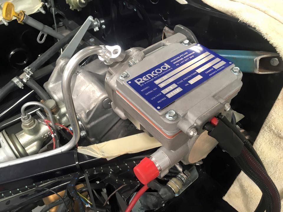 Rencool electric compressor and refrigerant hoses installed in a vehicle engine bay.